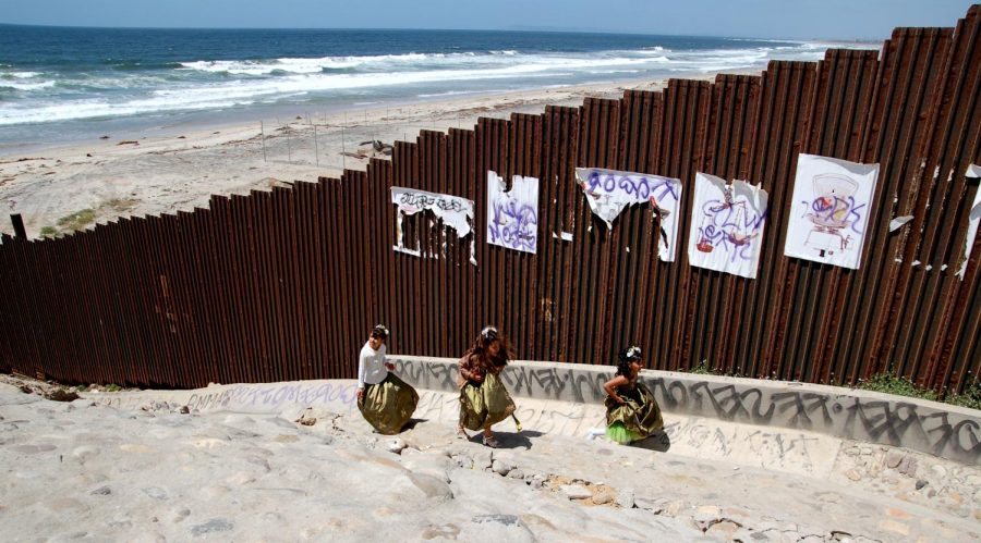 The+Forgotten+Ones.+Playing+alongside+the+wall%2C+three+little+girls+play+along+the+US%2FMexican+border+at+Tijuana+Beach%2C+in+Baja+California%2C+Mexico.+Beknownstingly%2C+it+is+unknown+of+where+these+girls+came+from+or+if+they+are+parentless.+Unfortunately%2C+these+girls+are+a+small+amount+of+the+millions+of+the+children+that+were+left+parentless+during+the+procession+of+migrants.