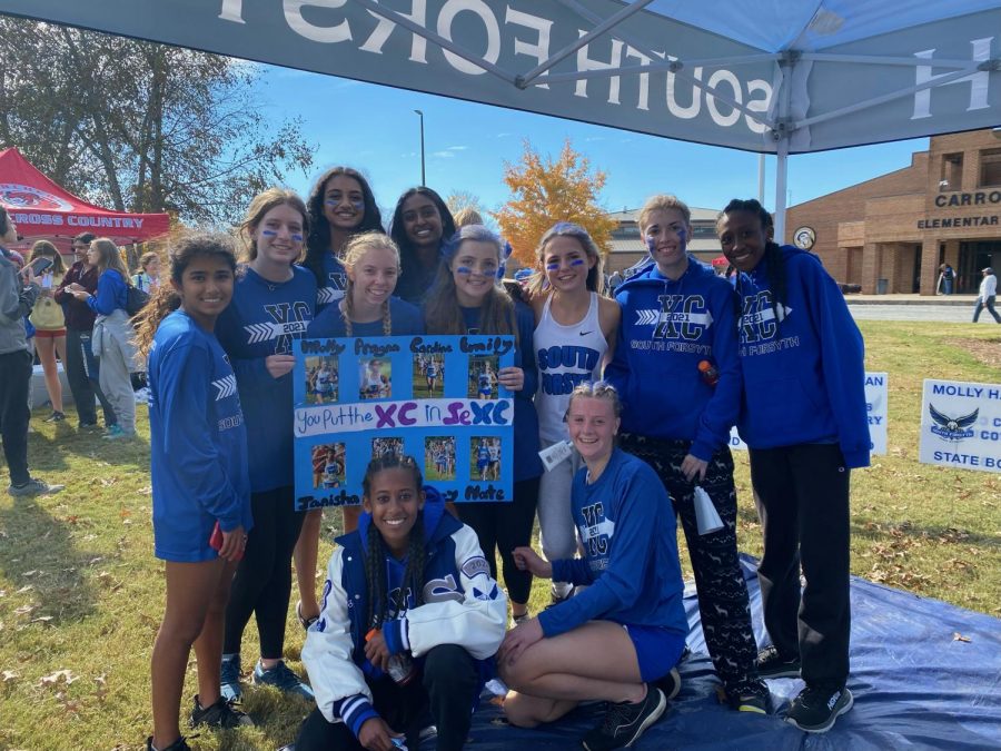 Varsity girls. As the varsity girls get ready to run, their teammates hold up signs to cheer them on. Junior varsity (Jv) runners along with returning alumni helped make signs for each varsity runner.